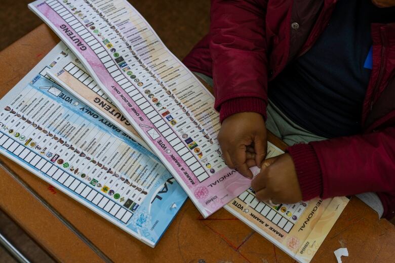 Long sheets of paper are shown resting on a table as a person's hands are shown handling them.