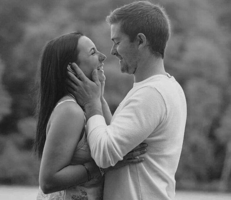 A black and white photo of a young man and woman. They're embracing, with the man cradling the woman's face as she smiles.