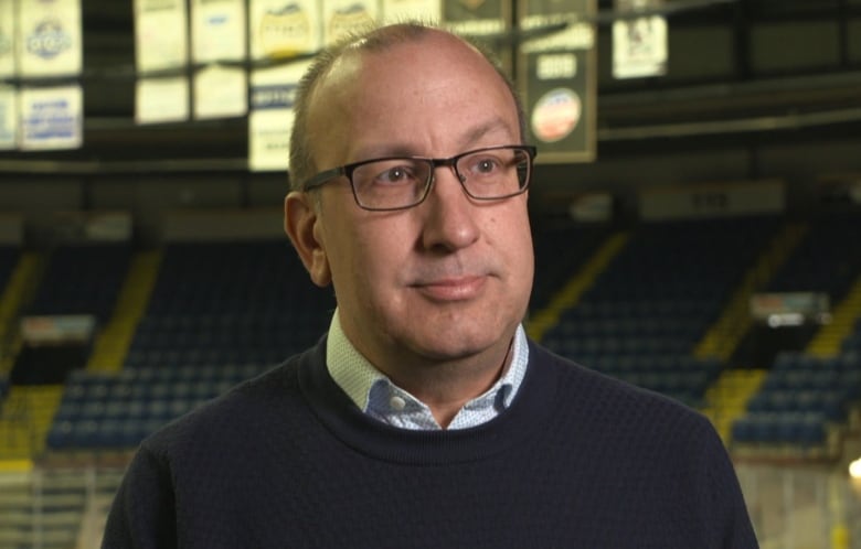 A man wearing a black sweater and glasses standing inside an empty arena. 