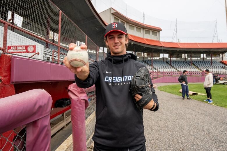 A baseball player poses with a ball. 