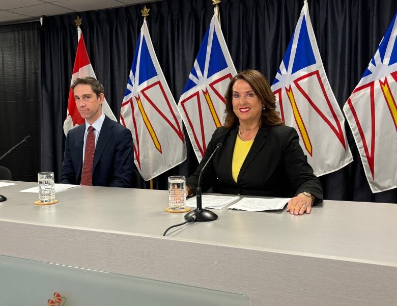 Two politicians sit behind a table in a media briefing room. 