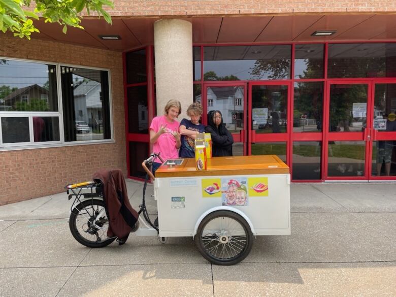 Three teens pose behind an ice cream trike.