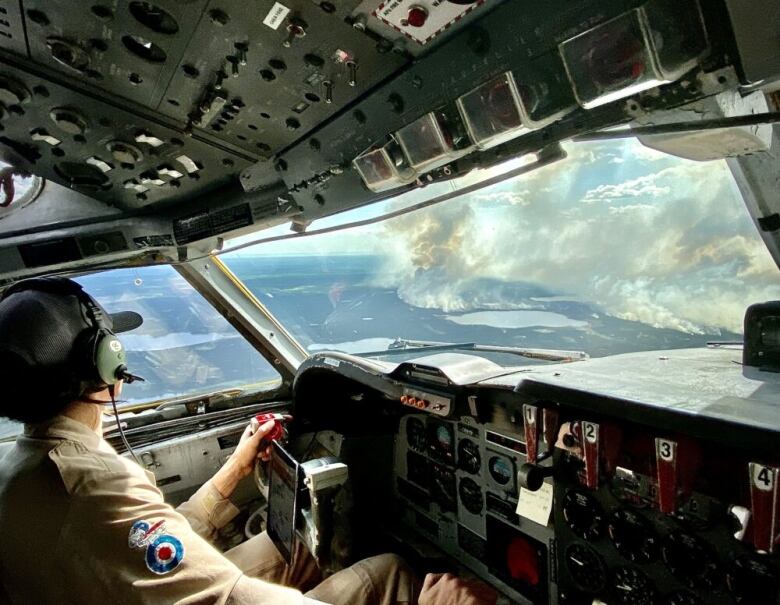 A pilot sits behind the controls of a plane. Smoky sky is visible in the background 