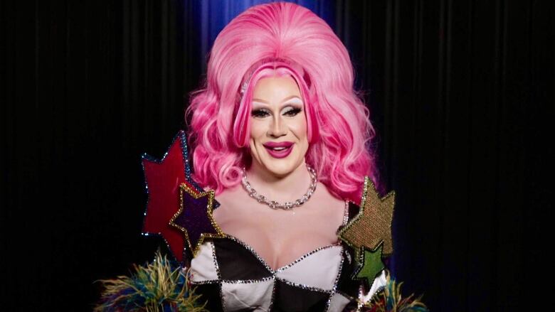 A drag queen wears a pink wig and checkered dress.