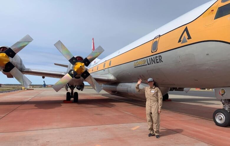 A female pilot stands beside a large plane. 