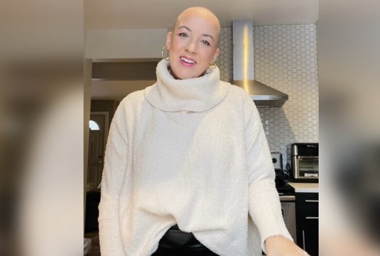 A woman smiles while wearing bright pink lipstick and a white turtleneck sweater in a kitchen. 