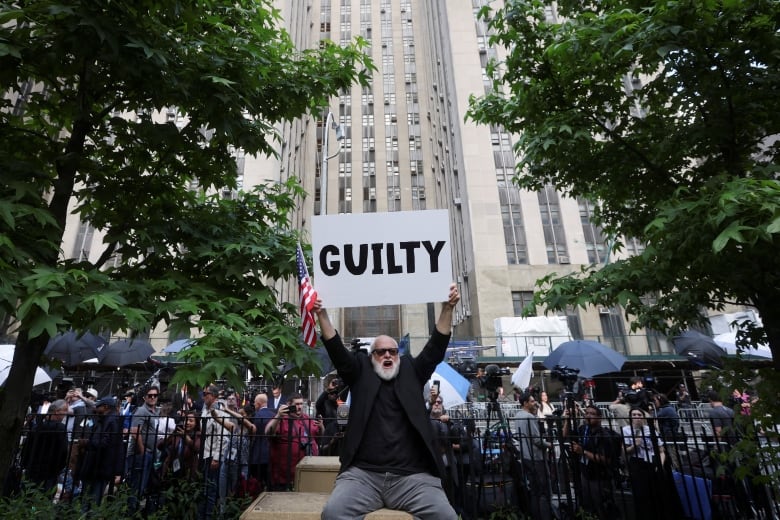 A man in a black shirt holds up an American flag and a white sign that says 