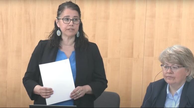 Woman in blazer stands with paper in hand.