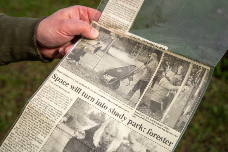 A hand is seen holding a laminated newspaper article, featuring text and black and white photos.