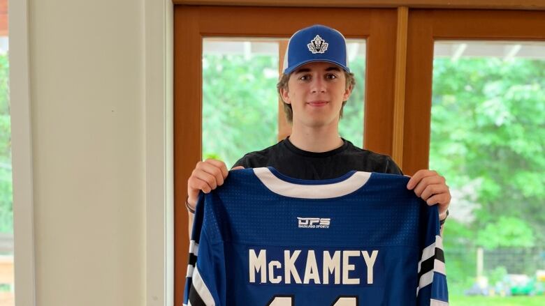 A young boy holds up a blue hockey jersey with his name on it