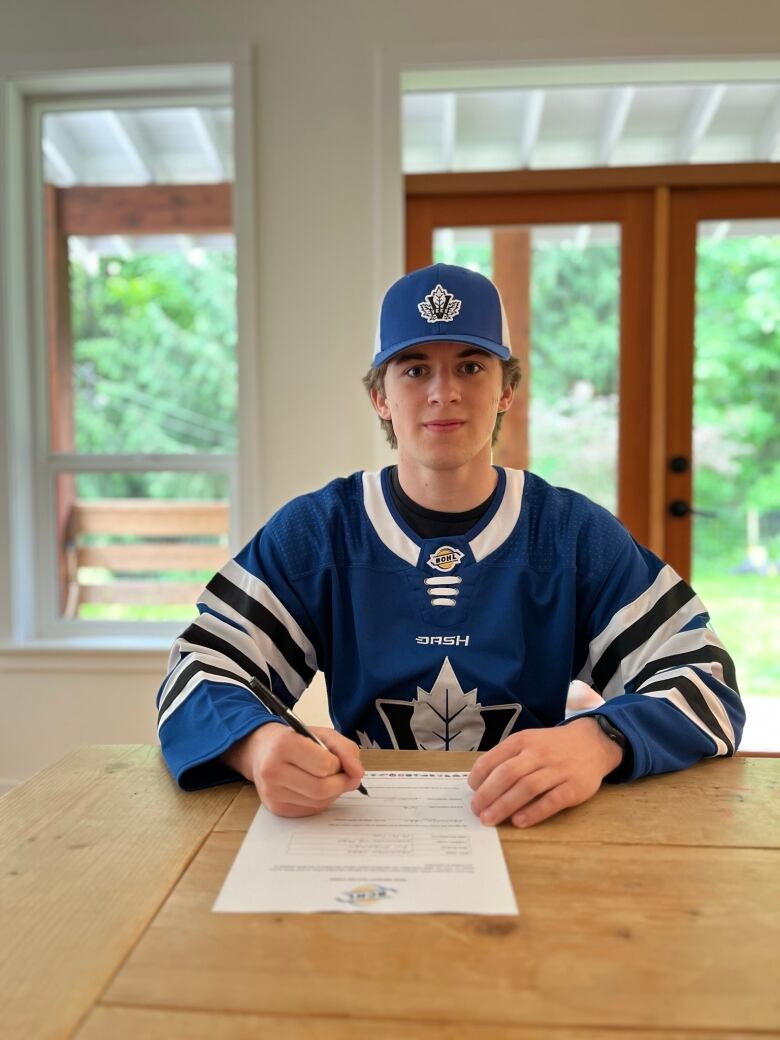 A boy sits at a desk to sign a document