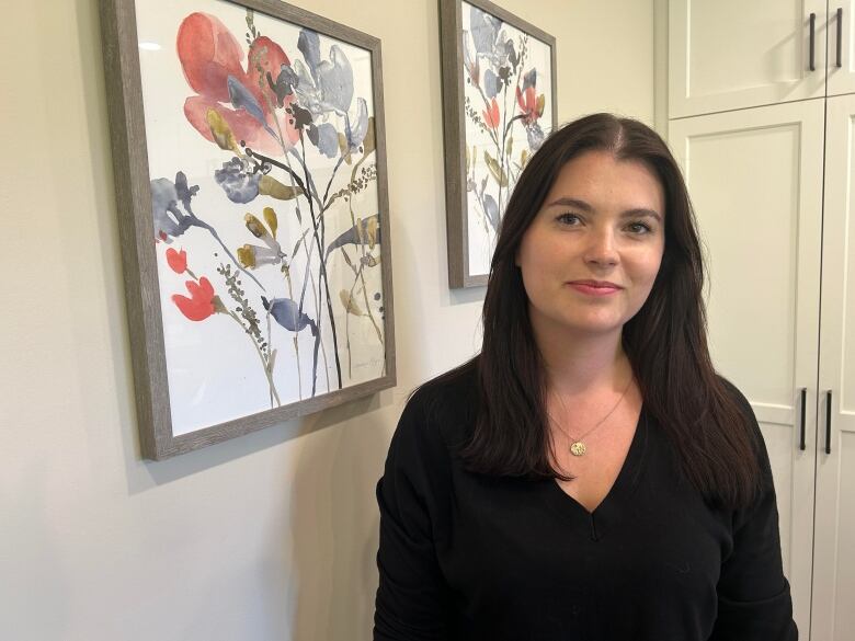 A woman stands in front of two paintings of flowers in her home.