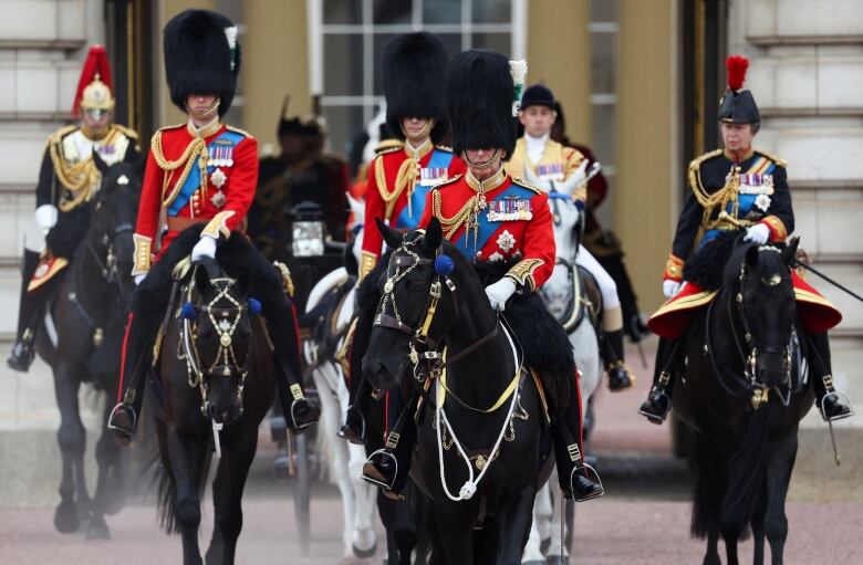 Several people wearing military uniforms ride horses as part of a ceremonial event.