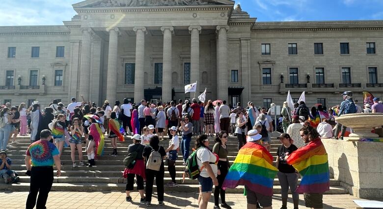 A group of people are pictured standing on stairs, with some wearing rainbow-coloured flags.