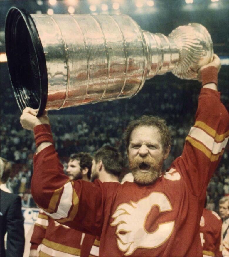 A man wearing a red hockey jersey is pictured holding a trophy. 