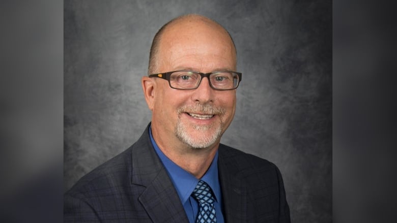 A man wearing glasses and a suit smiles to the camera.