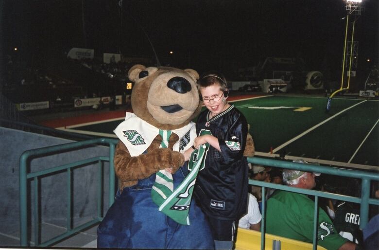 A boy in glasses and a black jersey stands next to a person dressed in a gopher costume.