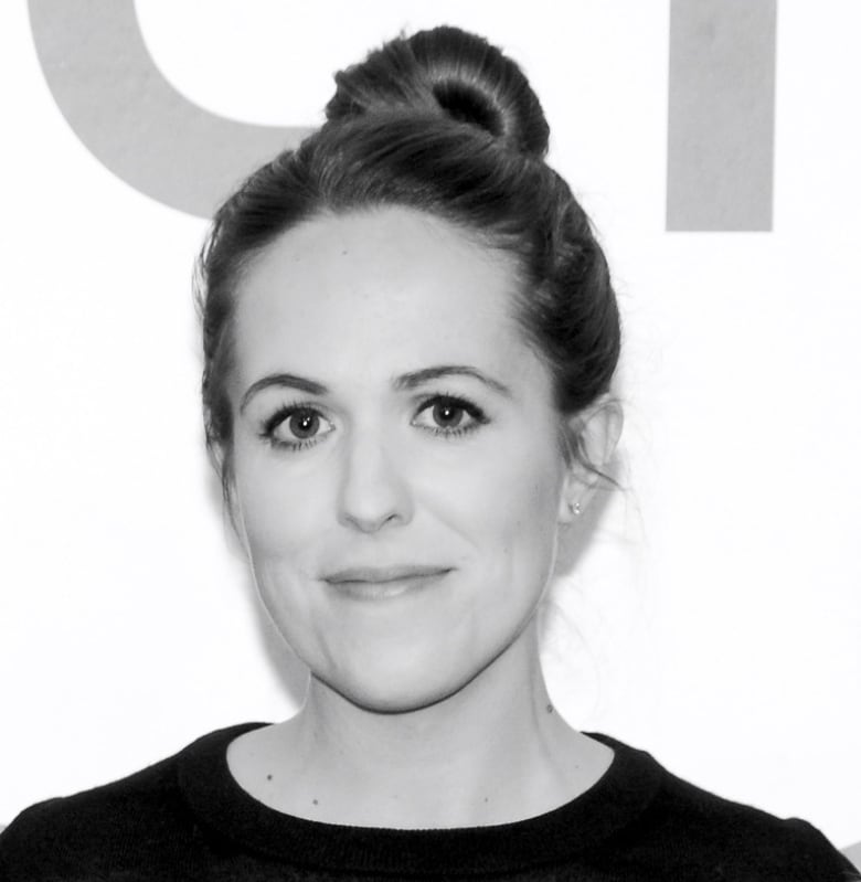 A black and white photo of a woman with dark hair and a black shirt, smiling for the camera