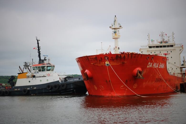 A tugboat works to undock a large orange oil tanker. 