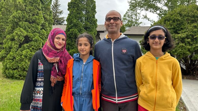 A family of four stands in front of a house.