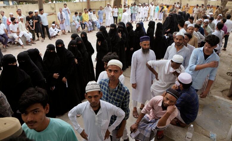 Women wearing long black robes and veils, and men stand in line to vote.