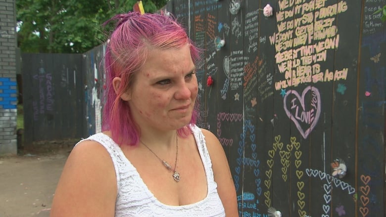 A woman stands in front of a fence decorated with words and pictures.