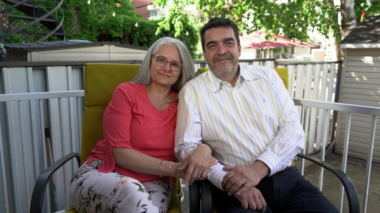 A woman and man link arms while seated on a porch.