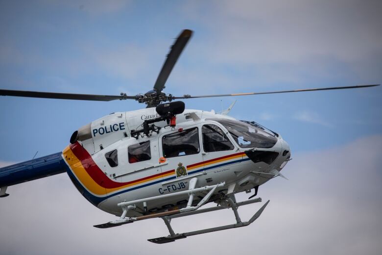 A helicopter with RCMP regalia, including a logo, is pictured in the sky.