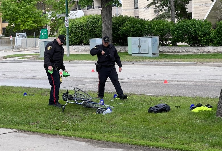 Officers put colourful markers around a damaged bicycle on a grassy boulevard.