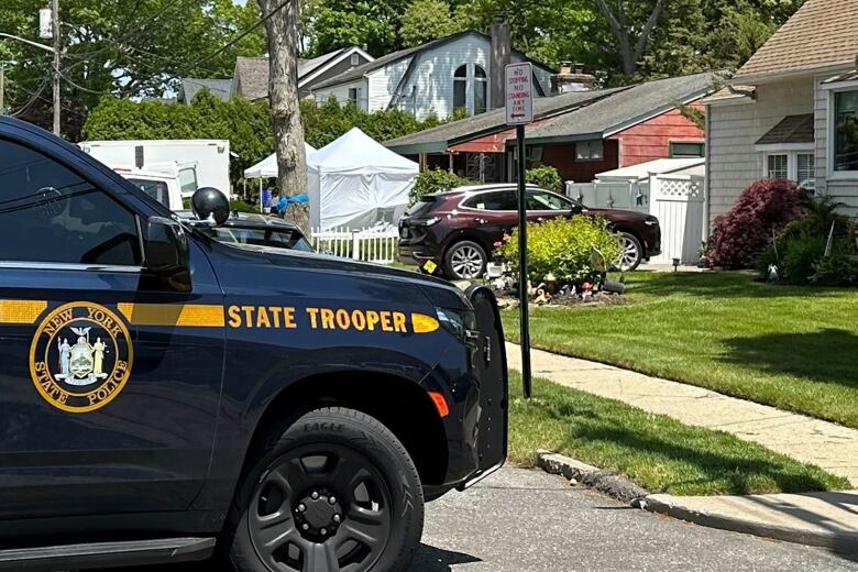 White tents in the front yard of a house with a blue SUV marked state trooper in the foreground.