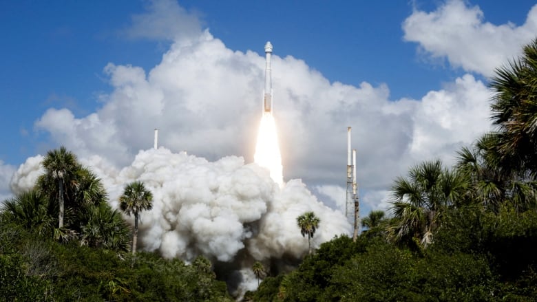 A white rocket leaves a fiery trail as it lifts off into a blue sky dotted with clouds.