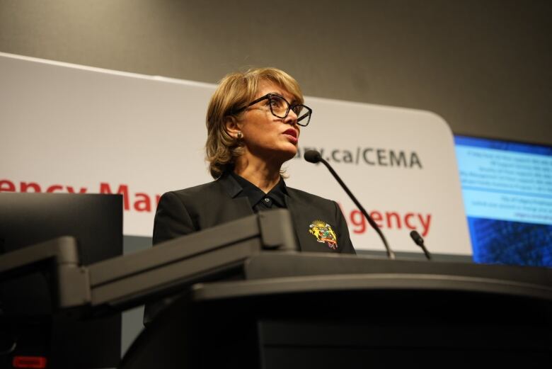 a woman with glasses speaks into a microphone 