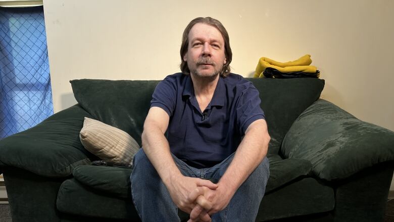 A man with shaggy brown hair sits on a couch.