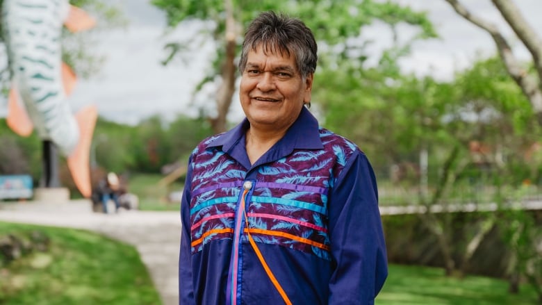 A person wearing a purple ribbon shirt stands in a park.