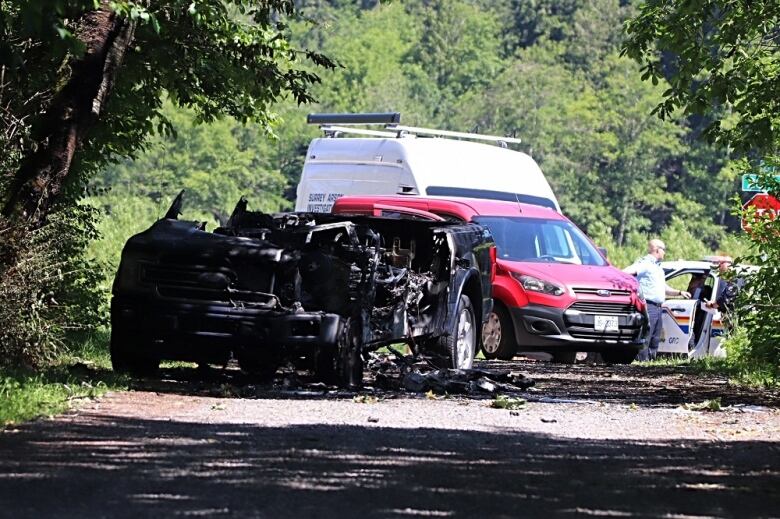 A burned vehicle in front of a red car.