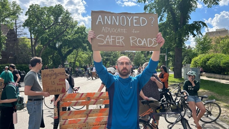 A man holding a sign that says, 'Annoyed? Advocate for safer roads.' 