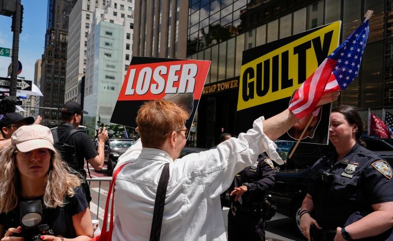 Demonstrators move about on a city street, brandishing American flags and placards reading 'loser' and 'guilty.'