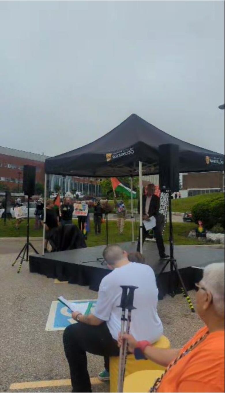 Protesters with flags and signs behind a make-shift stage.