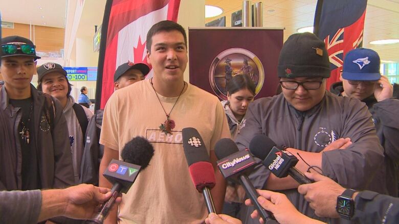 A young man speaking in front of several mics.