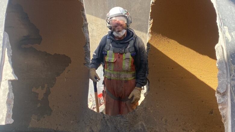 A man stands in between a half-cut concrete pipe. 