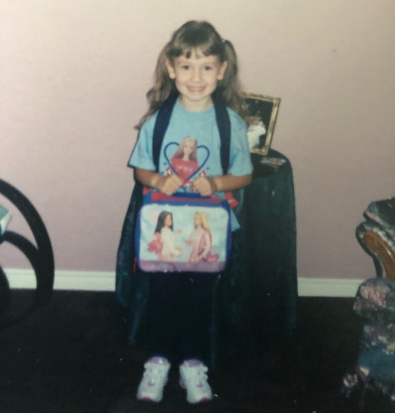 A girl wearing a blue shirt and holding a blue lunch box. 