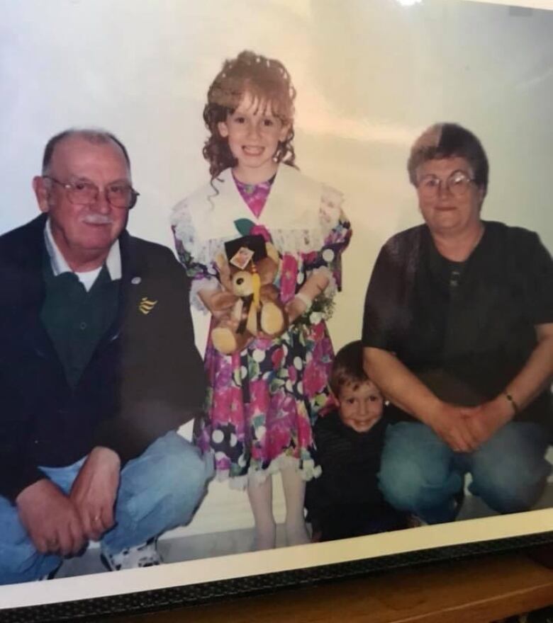 Two older people and a child stand near a white wall. 