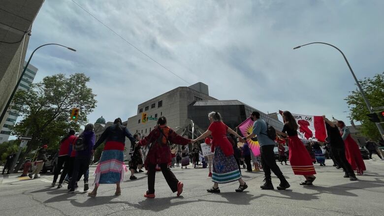 A number of people dance in a circle while holding hands.