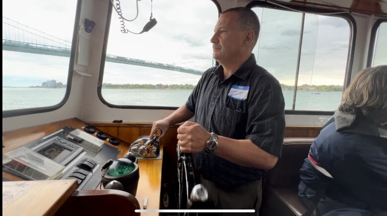 Man at the helm of a boat with steering wheel in hand. 