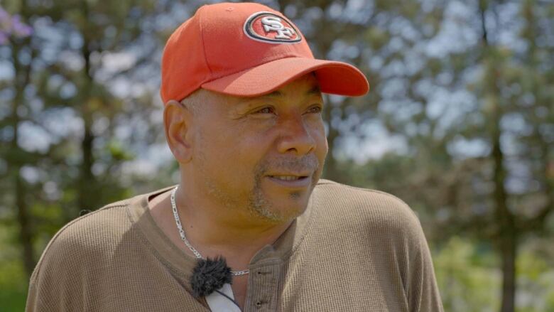 Man, looking away from camera while talking wearing a red hat.