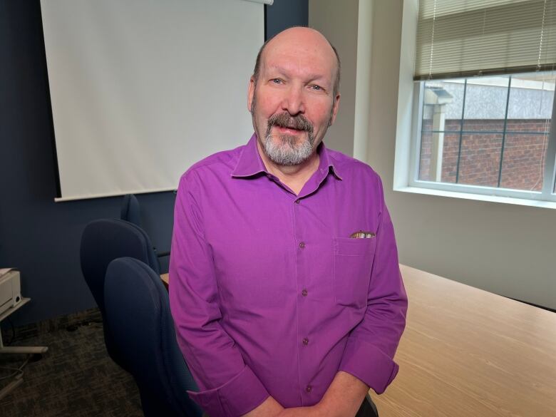 A portrait of a balding man wearing a purple shirt. 