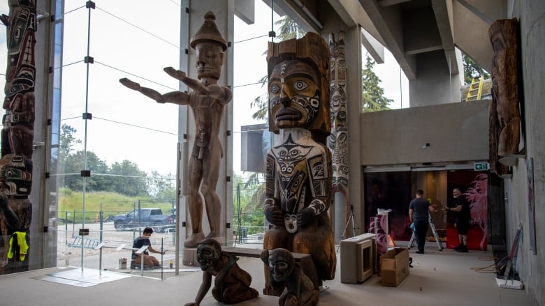 A series of totem poles and Indigenous artefacts in a museum, with construction workers around it.