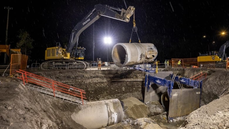 a large pipe is being lifted out of a deep hole with heavy duty machinery. it is nighttime and it is raining.