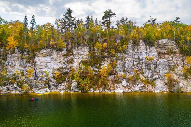 A kayaker is seen in the water next to rocky cliffs.