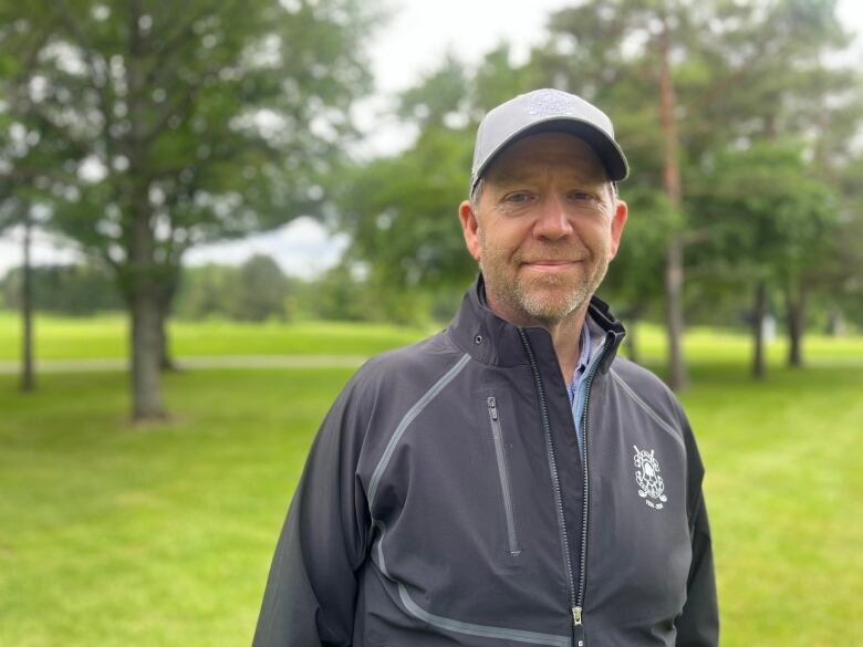 Man wearing cap and sports jacket stands on golf course. 